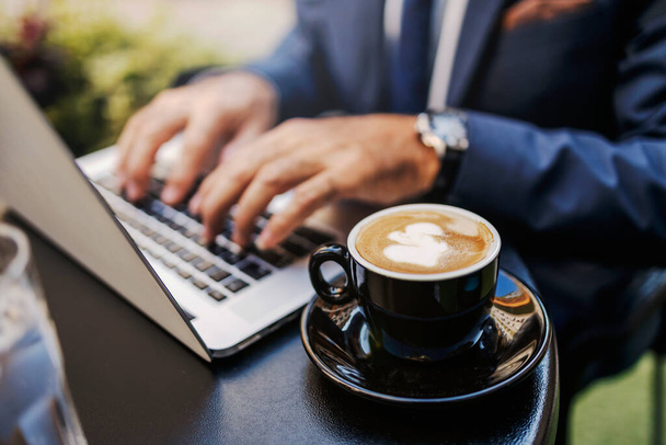 Close up of fresh espresso with foam. In the background, hands are typing on the laptop. Selective focus on the cup of coffee. Coffee for a busy businessman. - Photo, Image