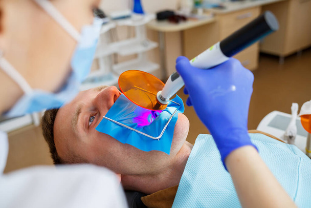 Mulher dentista examina a paciente com instrumentos na clínica odontológica. O médico faz tratamento dentário nos dentes de uma pessoa na cadeira do dentista. Foco seletivo - Foto, Imagem