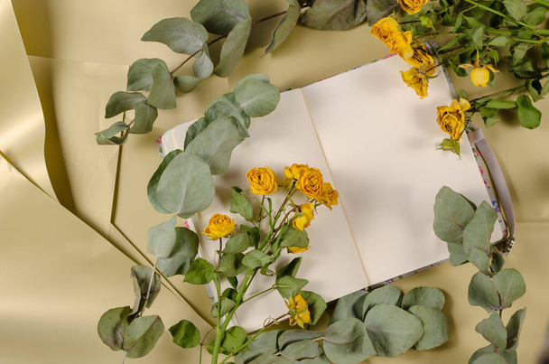 Gelbe Rosen, Eukalyptuszweige und ein offenes Notizbuch. Ansicht von oben. Selektiver Fokus. - Foto, Bild