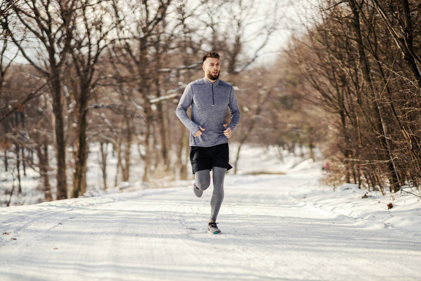 Человек бегает по заснеженной дорожке на природе, Зимний фитнес, фитнес на свежем воздухе, здоровый образ жизни. - Фото, изображение