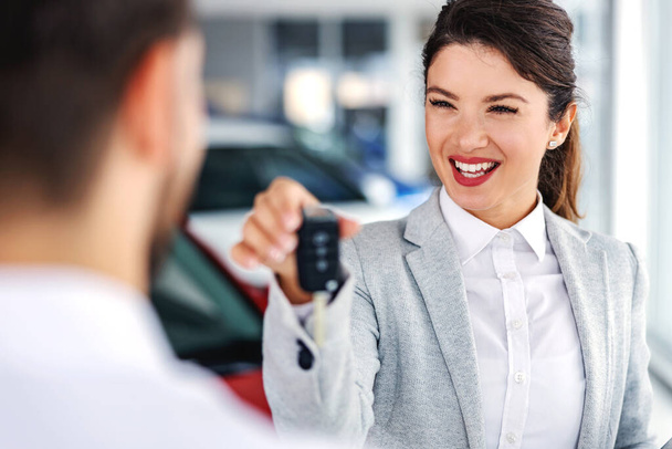 Sorrindo, vendedor de carros amigável em pé no salão de beleza do carro com um cliente e entregando-lhe as chaves do carro mais vendido. - Foto, Imagem