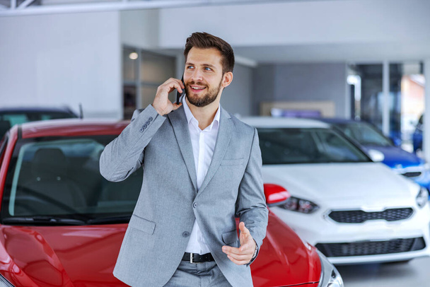 Hymyilevä, iloinen asiakas seisoo autosalongissa ja puhuu vaimolleen. Hän kehuskelee ostamallaan uudella autolla.. - Valokuva, kuva