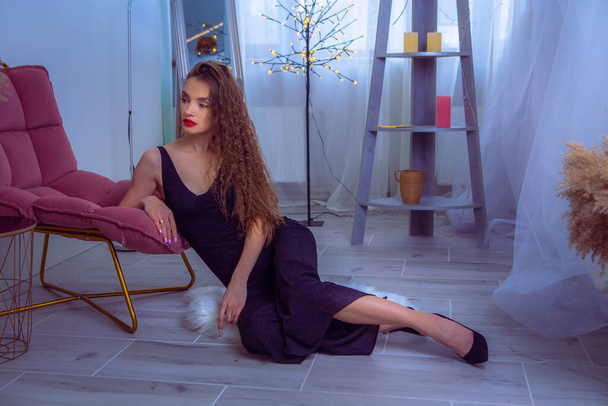 Glamour woman with red lips in black overalls sits on the floor at home and looking away - Fotó, kép