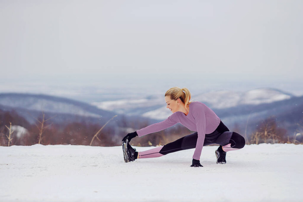 Стройная спортсменка в форме, занимающаяся разминкой и растяжкой на природе в снежный зимний день. Здоровые привычки, зимний фитнес - Фото, изображение