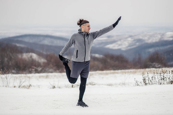 冬の雪の日に自然の中でストレッチ演習を行う形のスポーツマン。健康的な習慣、屋外フィットネス、冬のフィットネス - 写真・画像