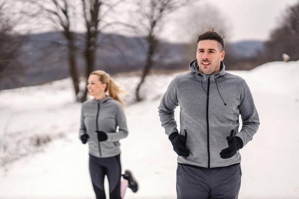 Αθλητής αγωνίζεται με τον φίλο του στη φύση σε χιονισμένη μέρα του χειμώνα. Χειμερινή φυσική κατάσταση, υγιεινή ζωή, φυσική κατάσταση - Φωτογραφία, εικόνα