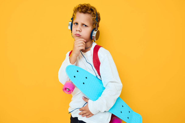 menino elegante com uma mochila vermelha usando fones de ouvido skate fundo amarelo - Foto, Imagem