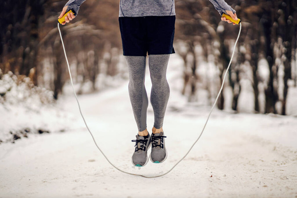 Nogi skaczące po linie po śnieżnej ścieżce zimą. Sporty zimowe, ćwiczenia wytrzymałościowe, zdrowe nawyki - Zdjęcie, obraz