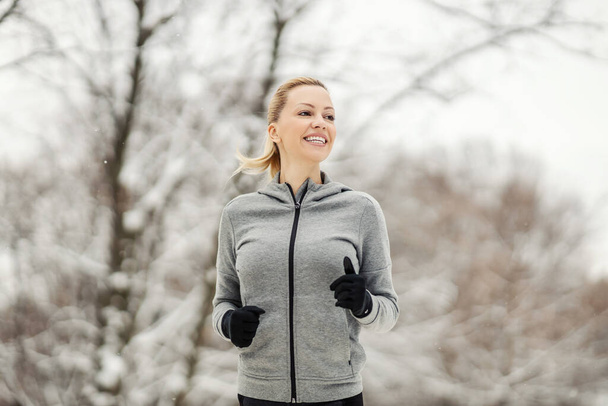 Boldog sportasszony kocog az erdőben havas téli napon. Egészséges életmód, szabadtéri fitness, téli fitness - Fotó, kép