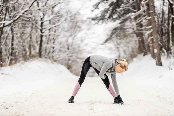 Deportiva de pie en el camino nevado en la naturaleza en invierno y haciendo ejercicios de estiramiento y calentamiento. Vida sana, aptitud invernal, aptitud al aire libre - Foto, imagen