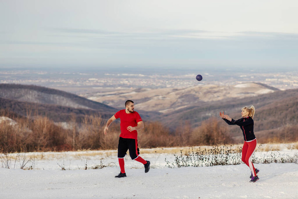 自然の中でジョギングし、雪の冬の日にフィットネスボールで投げ幸せなスポーティカップル。冬のフィットネス、健康的な生活、屋外フィットネス - 写真・画像