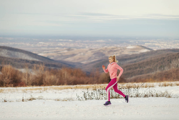 Sportswoman in shape running in nature at snowy winter day. Healthy habits, winter fitness, cardio exercises - Photo, Image