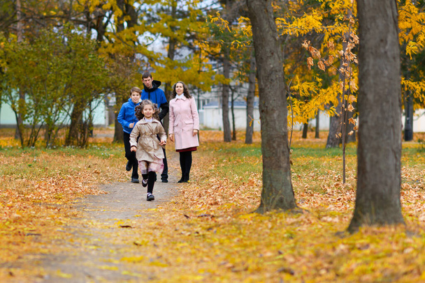Children run along path in autumn park. They play and laugh, they have a lot of fun. Beautiful nature and trees with yellow leaves. - Photo, Image