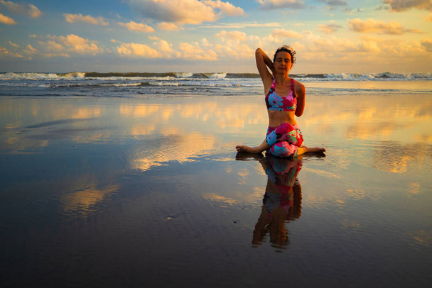 ビーチヨガ。護摩笠を実践する魅力的な女性。牛顔ポーズ。手を後ろに。肩の柔軟性。水の反射。禅の生活。セルフケアの概念。ヨガの隠れ家だ。コピースペース。インドネシアのバリ - 写真・画像