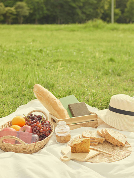 picknickconcept Er zitten veel dingen op de witte doek zoals brood, fruit, een flesje water, een hoed en een notitieboekje. - Foto, afbeelding