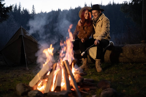 Vista frontale di turisti amorevoli seduti vicino a un fuoco acceso vicino a una tenda in un campeggio godendo di una bella notte d'autunno. Copia spazio. - Foto, immagini