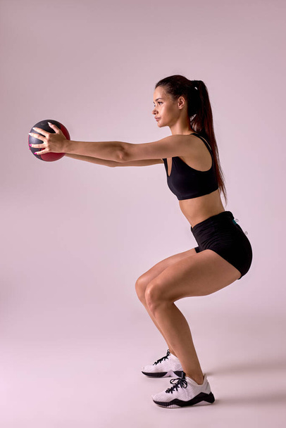 Side view portrait of Slim caucasian cross fit woman with fitness ball doing squats, isolated - Fotó, kép