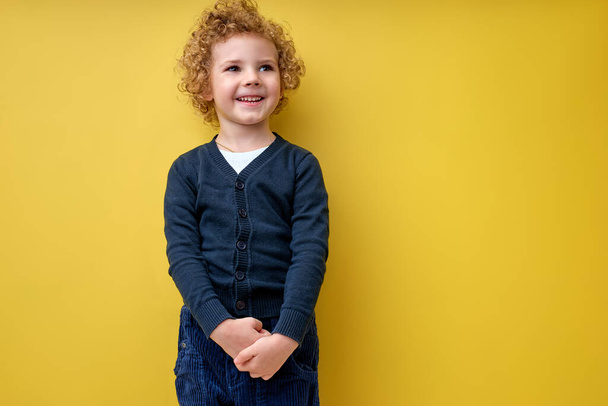 Portrait of child boy posing at camera isolated over yellow background in studio - Фото, изображение