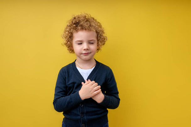 calm Cute kid boy hold hands on chest near heart. Human emotions concept - Фото, изображение