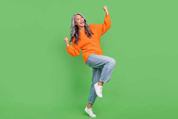 Full size photo of astonished white hair elder lady hands fists yell wear sweater jeans shoes isolated on green color background - Fotó, kép
