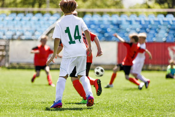 サッカースクールでゲームをプレイする子供たち。ユースチームのための夏のサッカートーナメント.草の上のボールのための高速かつ競争を実行している男の子ピッチ - 写真・画像