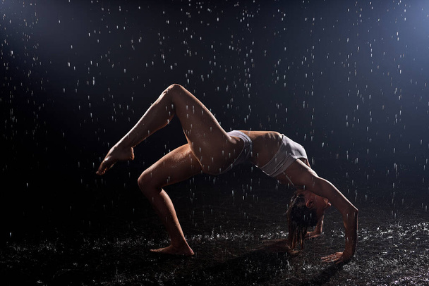 Silhouette of sexy Wet young woman in swimsuit dancing on floor under rain and splashes - Фото, зображення