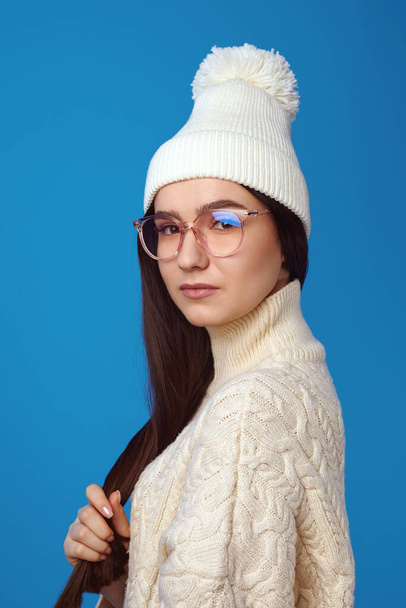Cute girl smiles at camera, wears white hat and knitted white oversized sweater - Foto, immagini