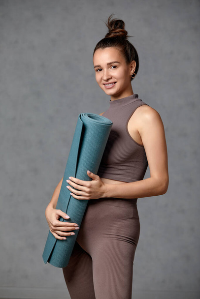 Smiling pregnant woman in sportswear ready for morning gymnastics or exercise. Happy young female follow healthy lifestyle during pregnancy, hold yoga mat for Pilates or stretching - Valokuva, kuva