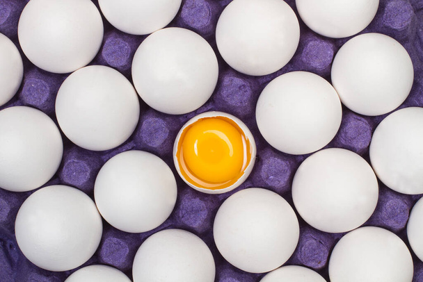 Huevos en una bandeja de cartón y un huevo roto en una vista cercana - Foto, imagen