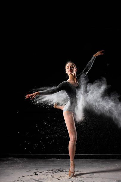 Beautiful ballerina woman in black bodysuit beautifully dances ballet in dark studio - Photo, image