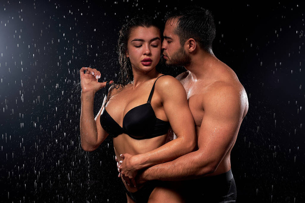 fit and wet passionate romantic couple hugging in water drops on black background - Photo, image