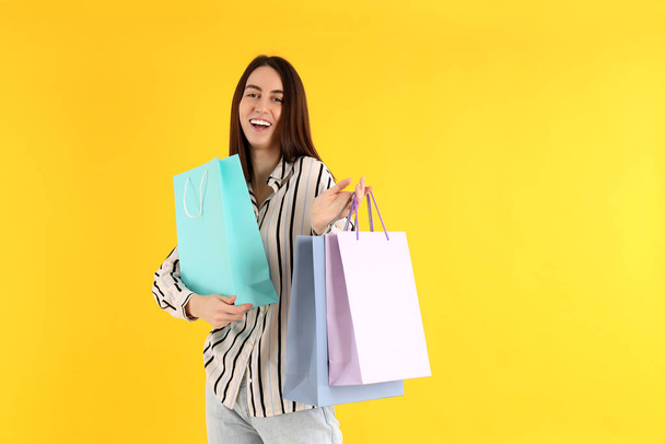 Attractive woman with shop bags on yellow background - Foto, imagen