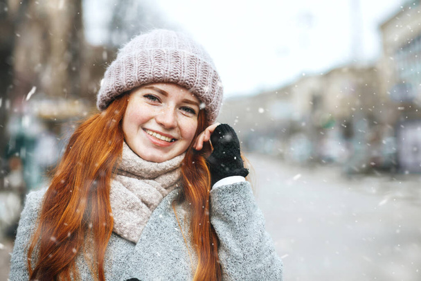 Забавная рыжая женщина носит пальто, гуляя по городу во время снегопада. Пространство для текста - Фото, изображение