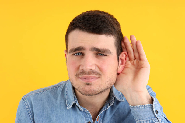 Mladý muž s problémy se sluchem na žlutém pozadí - Fotografie, Obrázek