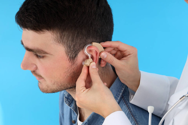 Dottore installa apparecchi acustici su orecchio giovane su sfondo blu - Foto, immagini