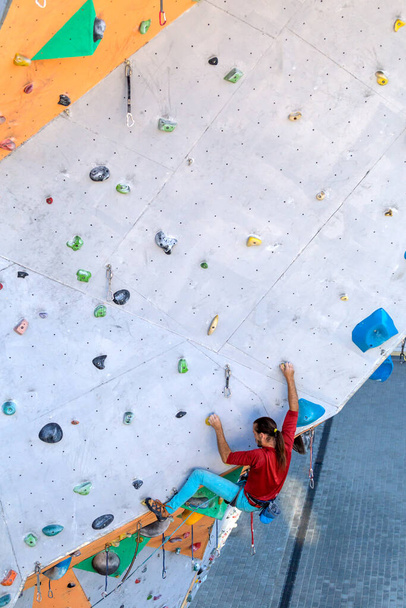 A man climbs a climbing wall, a climber is training on artificial terrain, rock climbing in the city, a strong man, sports in the city, safety in extreme sports. - Photo, Image