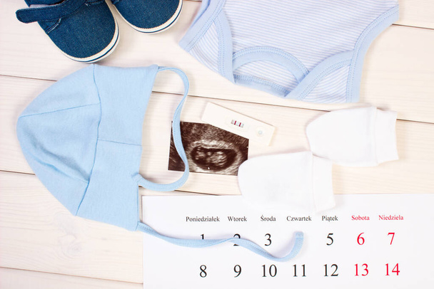 Pregnancy test with positive result, ultrasound scan of baby, clothing for newborn and calendar, concept of extending family and expecting for baby - Foto, immagini