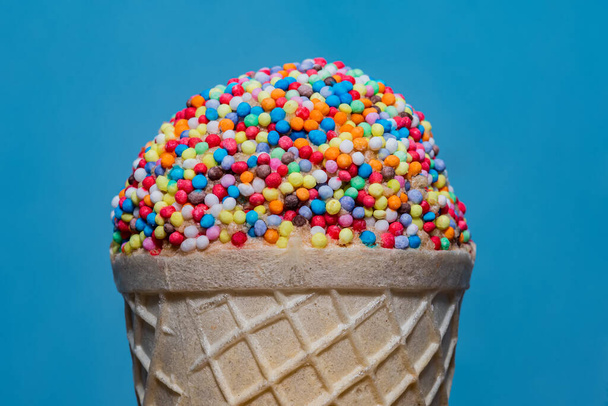 Конус мороженого с маленьким тортом, украшенным глазурью и круглыми брызгами с разбросанными брызгами. - Фото, изображение