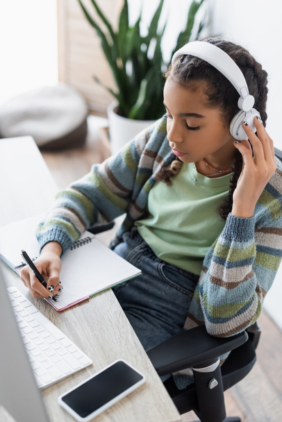 africký americký teenager psaní v notebooku při poslechu audio lekce ve sluchátkách - Fotografie, Obrázek