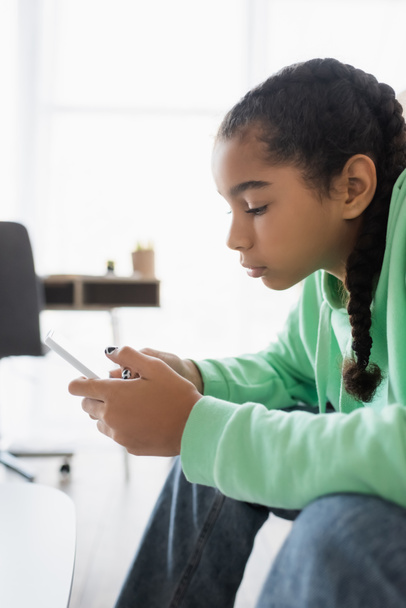 vista lateral de triste afro-americano adolescente menina conversando no telefone celular em casa - Foto, Imagem