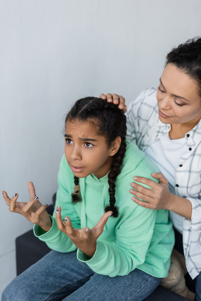 african american woman calming discouraged and gesturing daughter at home - Foto, Imagen