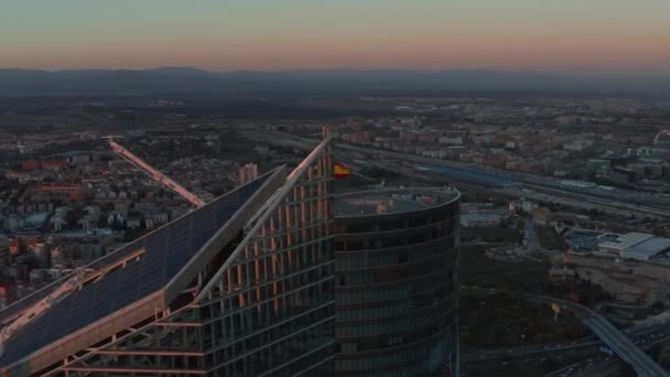Foto aérea de la parte superior de rascacielos en el centro de negocios CTBA. Bandera de España en la azotea. Ciudad al atardecer en el fondo. - Metraje, vídeo