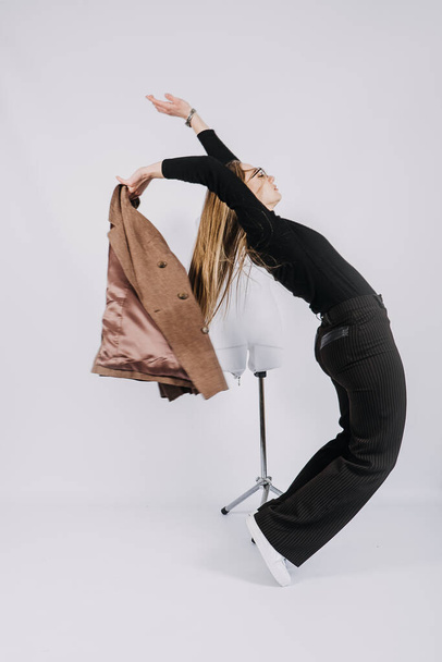 Full length studio portrait of exciting young woman fashion designer, stylist. Fashionable stylish blonde long hair girl in casual style cloth playing with chair - Fotó, kép