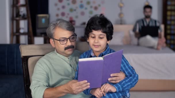 Ένας στοργικός παππούς και ο εγγονός του διαβάζουν ένα βιβλίο μαζί στο σπίτι - ελεύθερος χρόνος, οικογενειακός δεσμός, συνταξιοδότηση. Δεσμός μεταξύ γιου και παππού - Νυχτερινό πρόγραμμα, αφήγηση ιστοριών, καλές συνήθειες, στοργικός γιος - Πλάνα, βίντεο