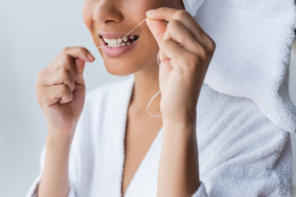 cropped view of smiling young african american woman in bathrobe flossing teeth in bathroom - 写真・画像