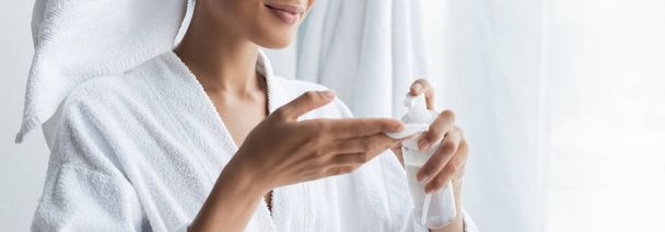 Afro-Amerikan kadının banyoda elinde temizleyici ve pamuklu bez şişeyle mutlu bir manzara, afiş. - Fotoğraf, Görsel