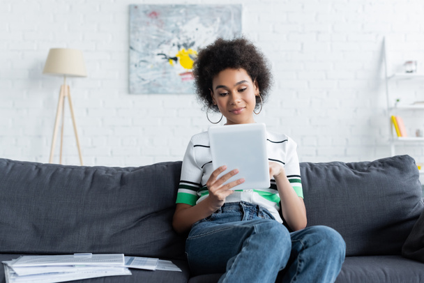 young african american woman using digital tablet while sitting on sofa  - Fotografie, Obrázek