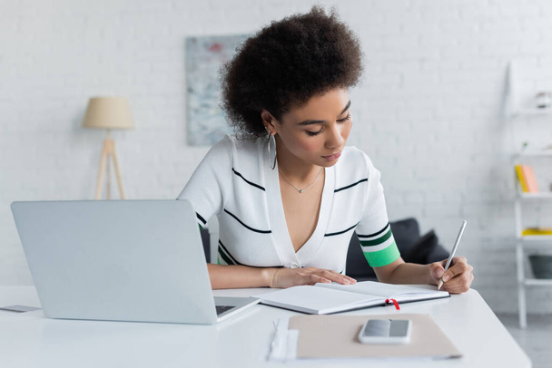 african american woman writing on notebook near gadgets  - Foto, immagini
