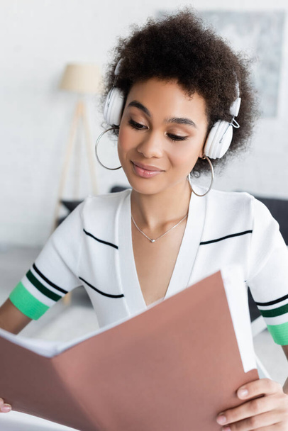 happy african american woman in wireless headphones looking at folder - Photo, Image