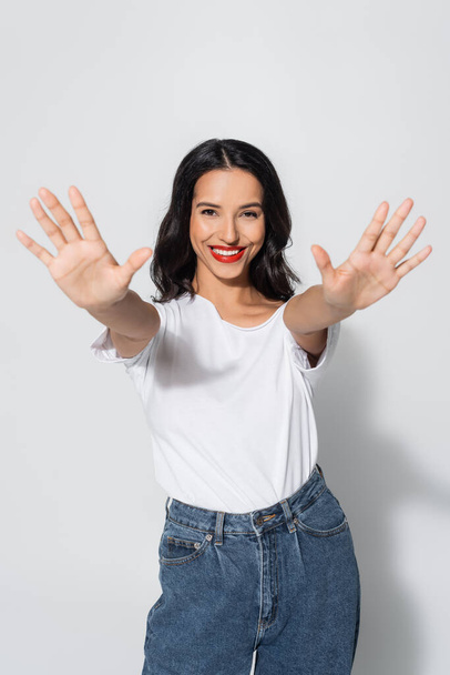 smiling brunette woman in white t-shirt posing with outstretched hands on grey - Foto, imagen